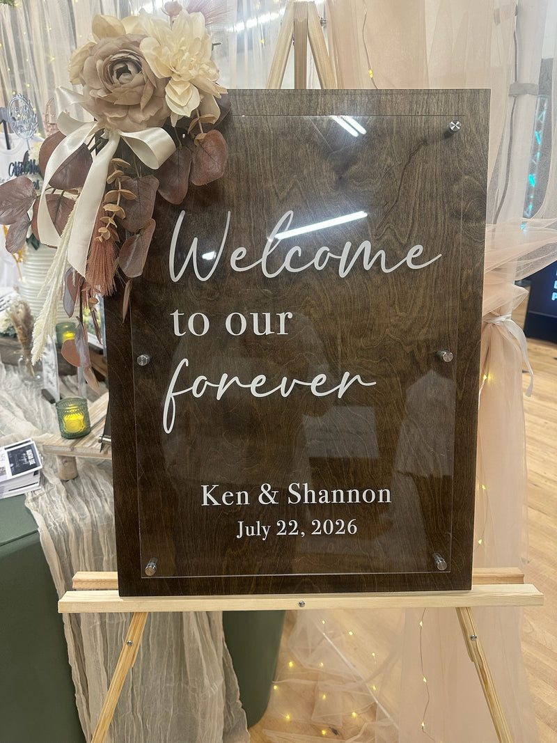 Decorative sign with 'Welcome to our forever' text on a stand with floral decorations.