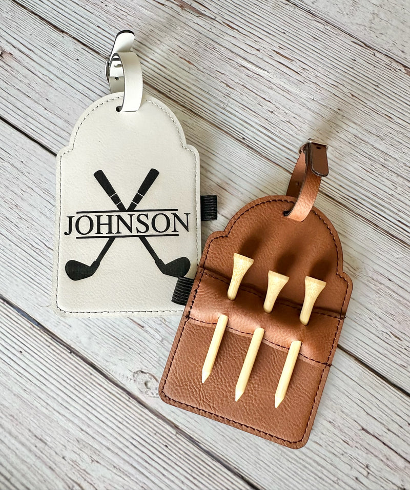 Brown leather case with golf tees and a white tag with 'JOHNSON' and golf club design on a wooden surface.