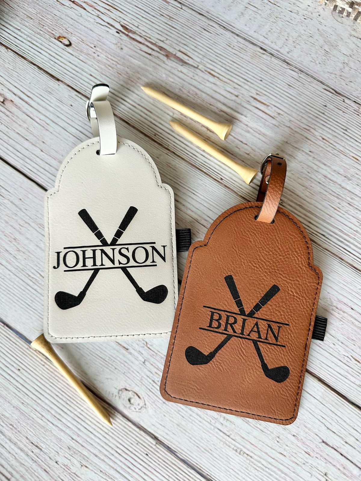 Two luggage tags with crossed golf clubs and names 'Johnson' and 'Brian' on a wooden surface.