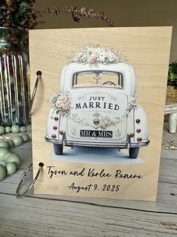 Decorative sign with a vintage car illustration and 'Just Married' text on a wooden background.