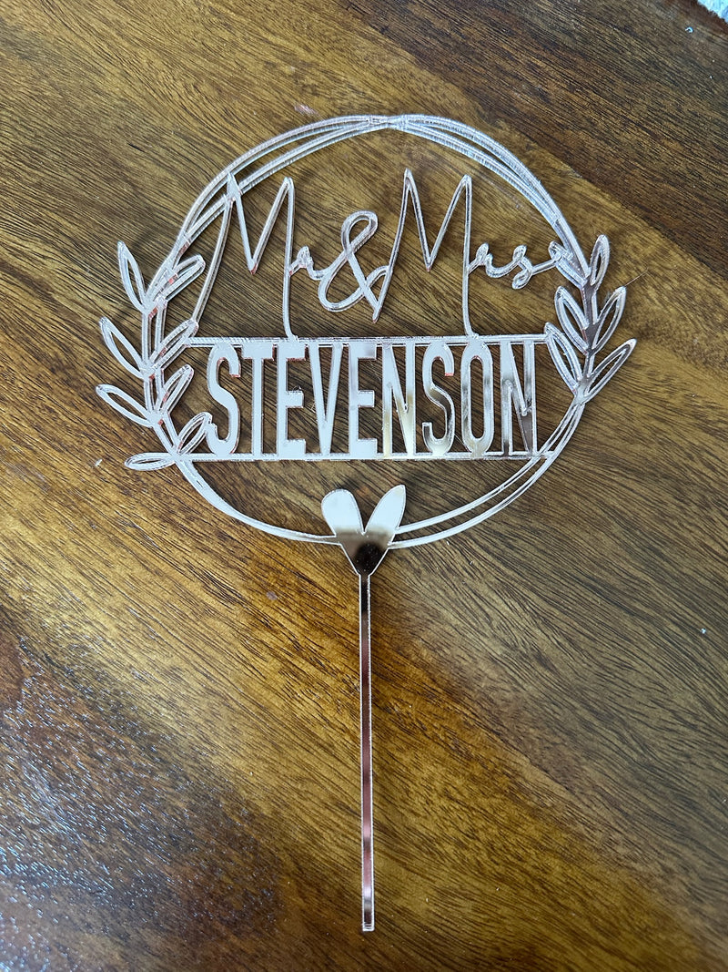 Decorative cake topper with 'Mr & Mrs Stevenson' on a wooden surface