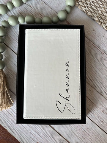 White embroidered name card with 'Shannon' on a wooden surface with beads and a tassel.